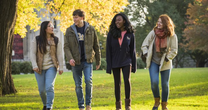 Four Pitt students walking on grass in Fall