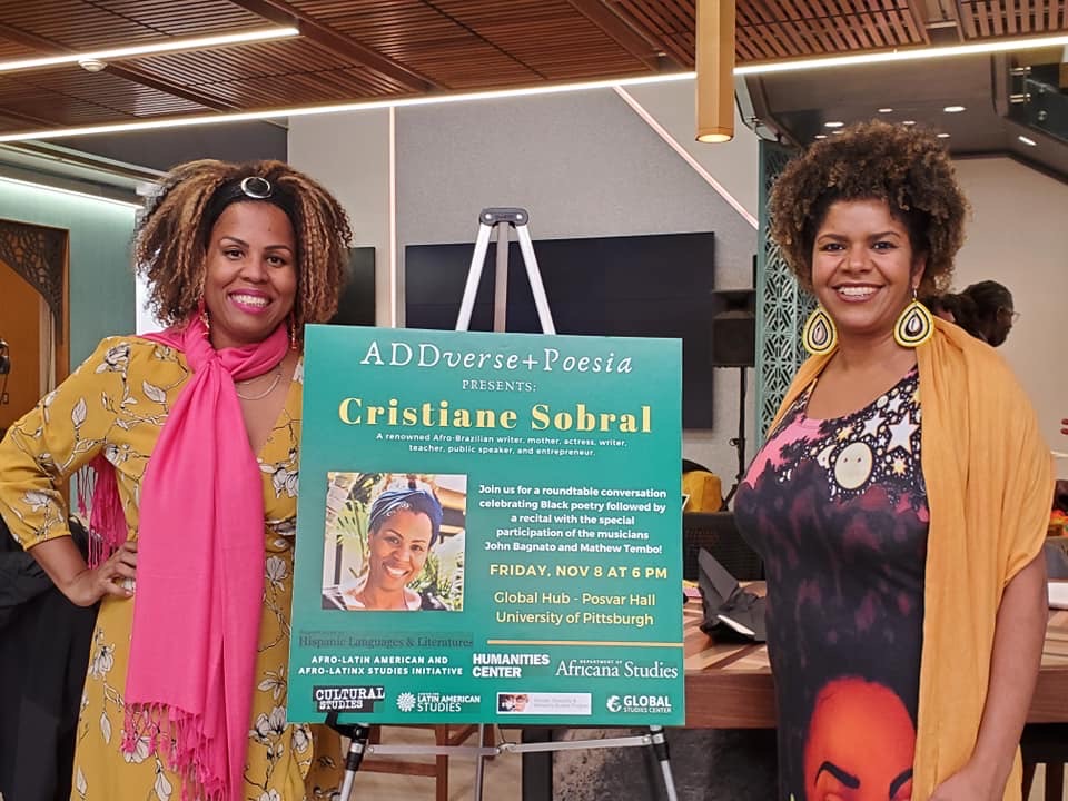 two guests standing next to event poster - ADDverse+Poesia presents: Cristiane Sobral