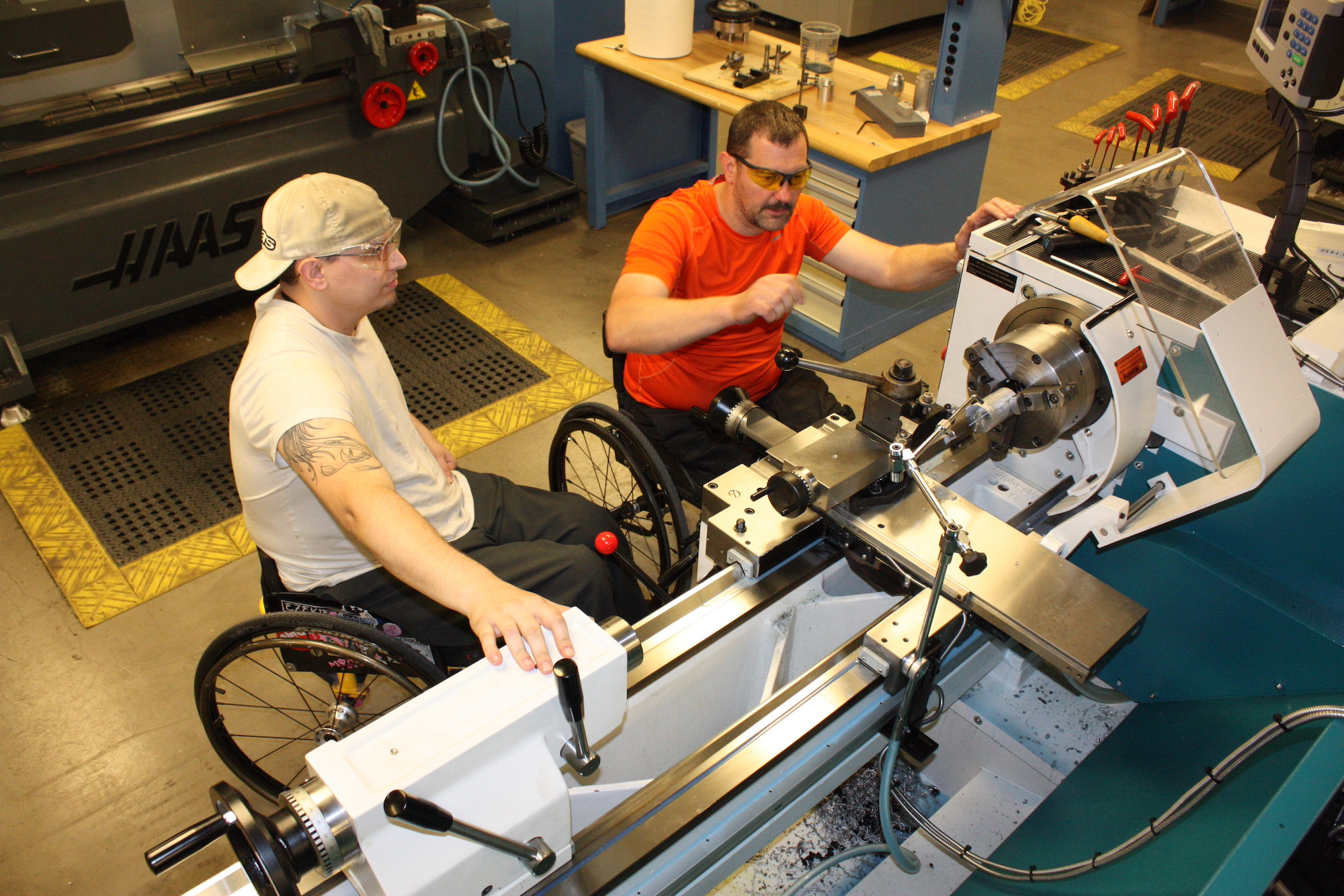 two men in wheelchairs working on lab machines 