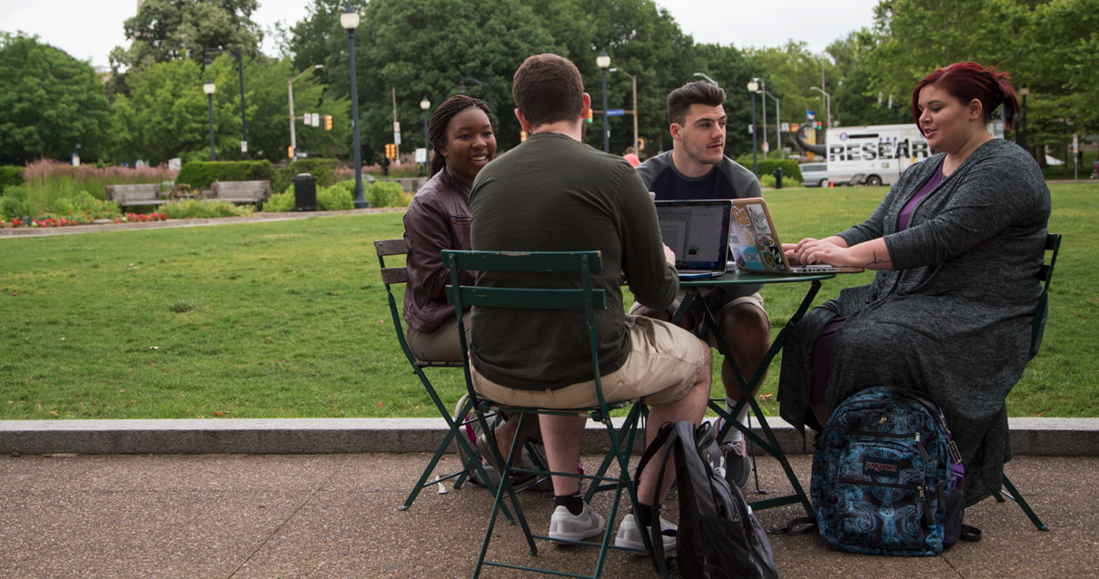 Four students sitting at a table outside talking