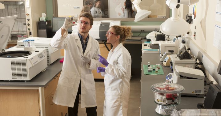 Two students wearing lab coats and gloves in lab