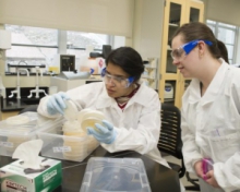 Students working in lab wearing white coat and goggles
