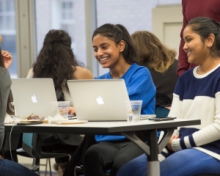 two students sitting around a table with macbooks